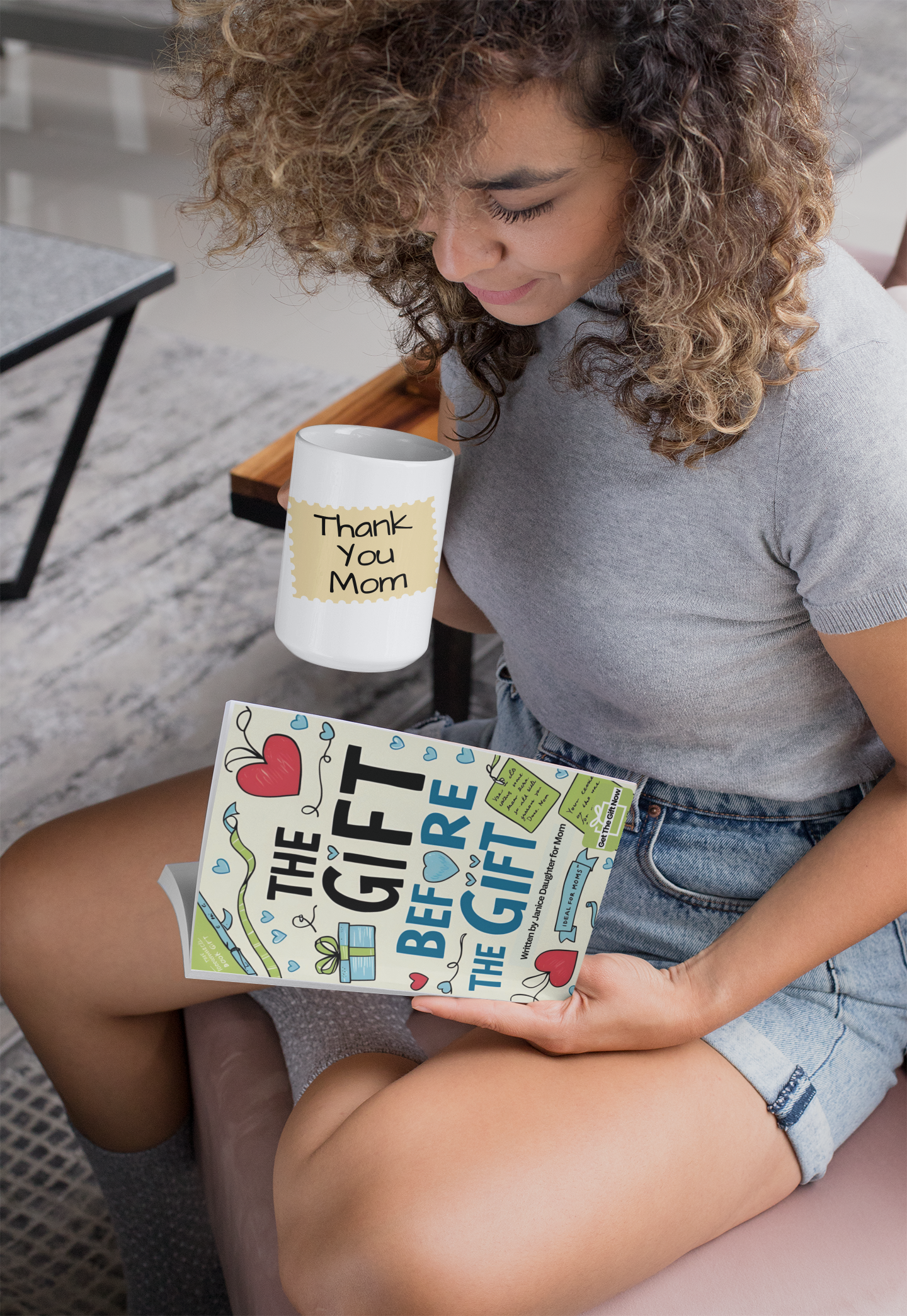 Woman smiling while holding a 'Thank You Mom' mug and a mini-book titled The Gift Before the Gift.