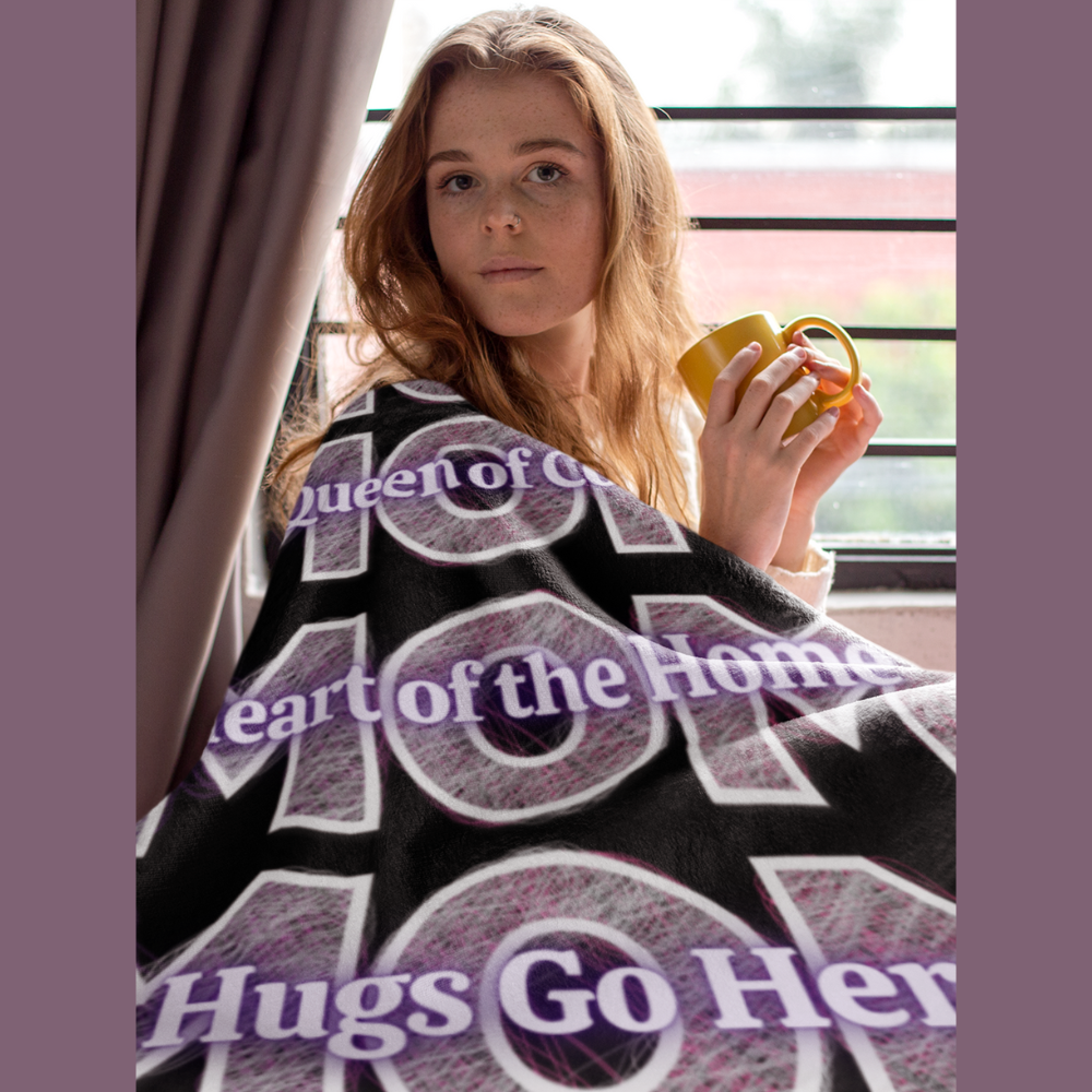 Woman wrapped in a cozy &quot;MOM&quot; blanket featuring loving affirmations like &quot;Queen of Cozy&quot; and &quot;Heart of the Home&quot; — a heartfelt Mother’s Day gift.